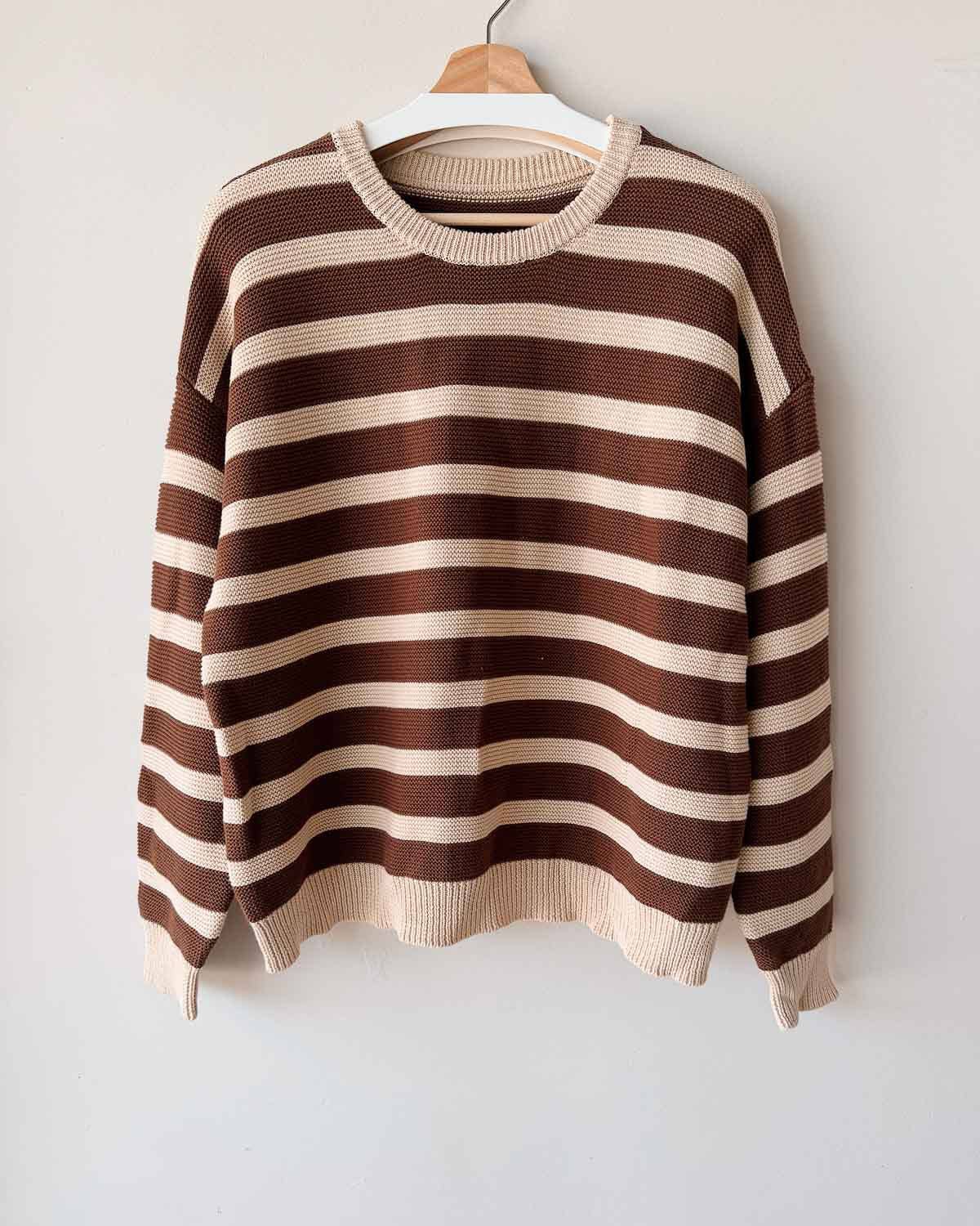Brown and beige striped sweater on a hanger against a white background