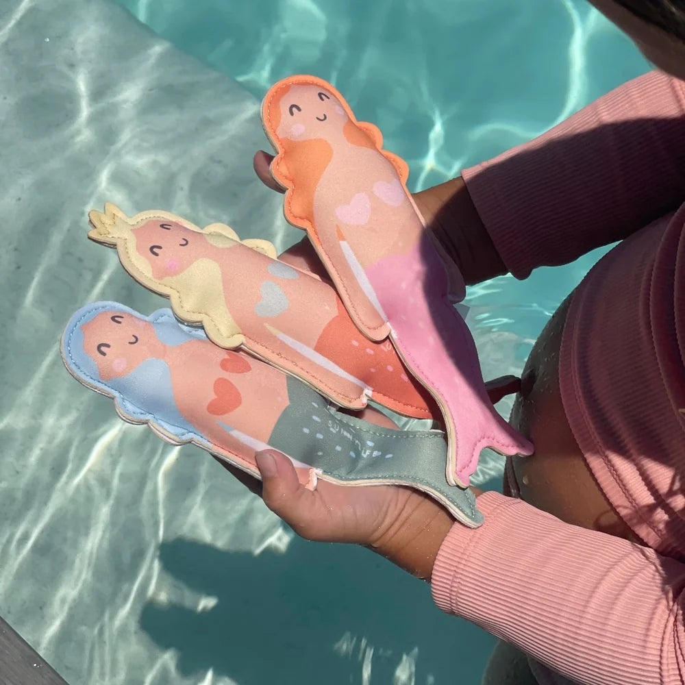 Three colorful mermaid-shaped toys held by a person against a pool background