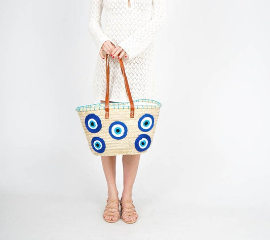 Person holding a woven bag with blue eye patterns on a white background