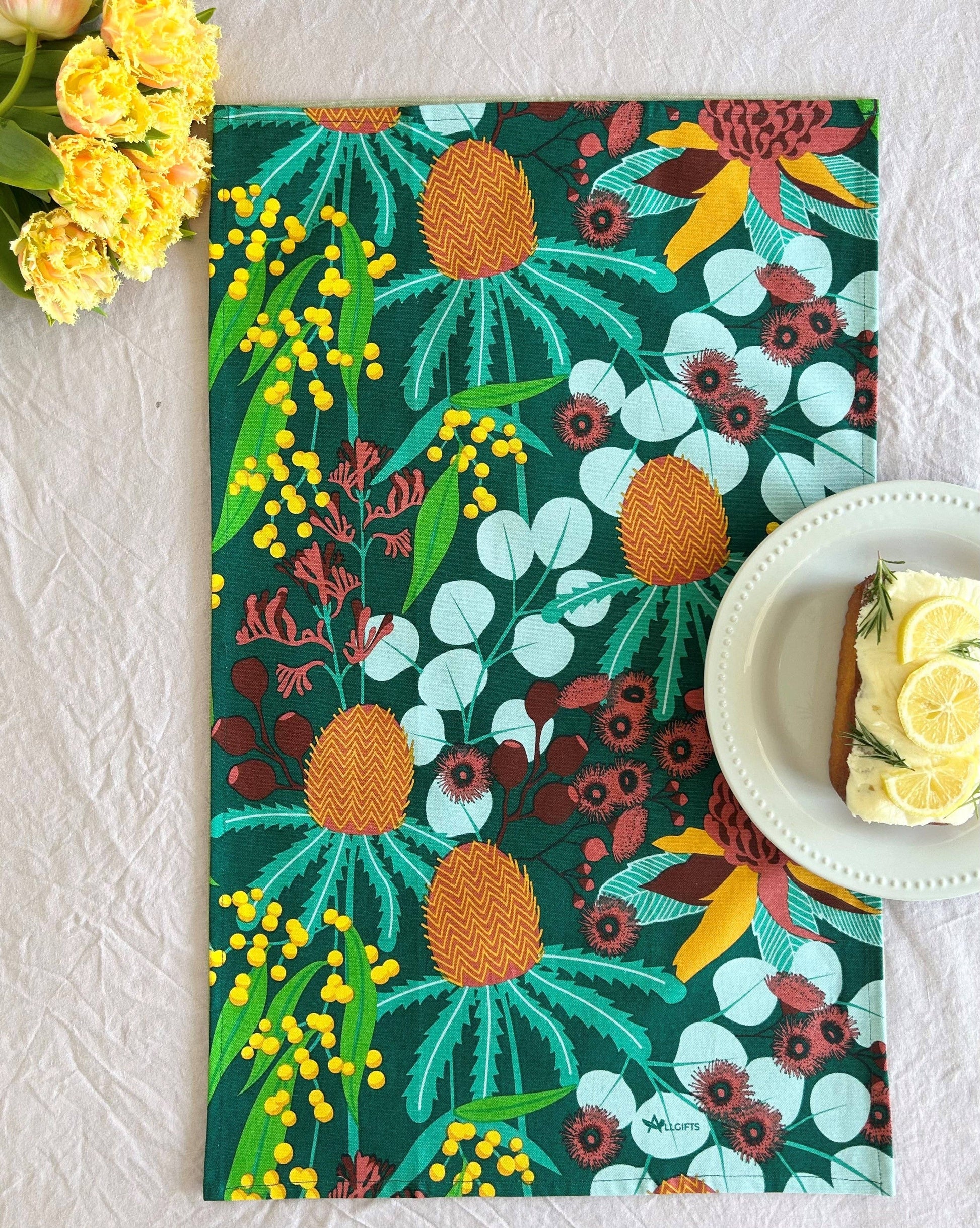 Colorful floral and pineapple patterned placemat on a textured surface with a cake and flowers.