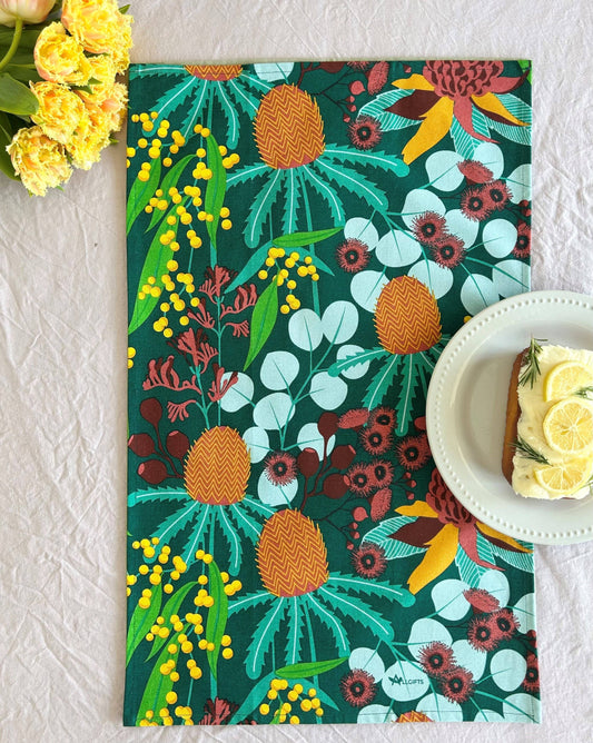 Colorful floral and pineapple patterned placemat on a textured surface with a cake and flowers.