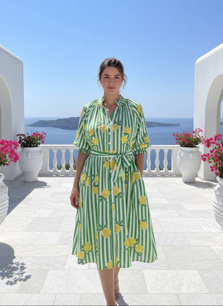 Woman in a green and yellow dress standing on a balcony with ocean view