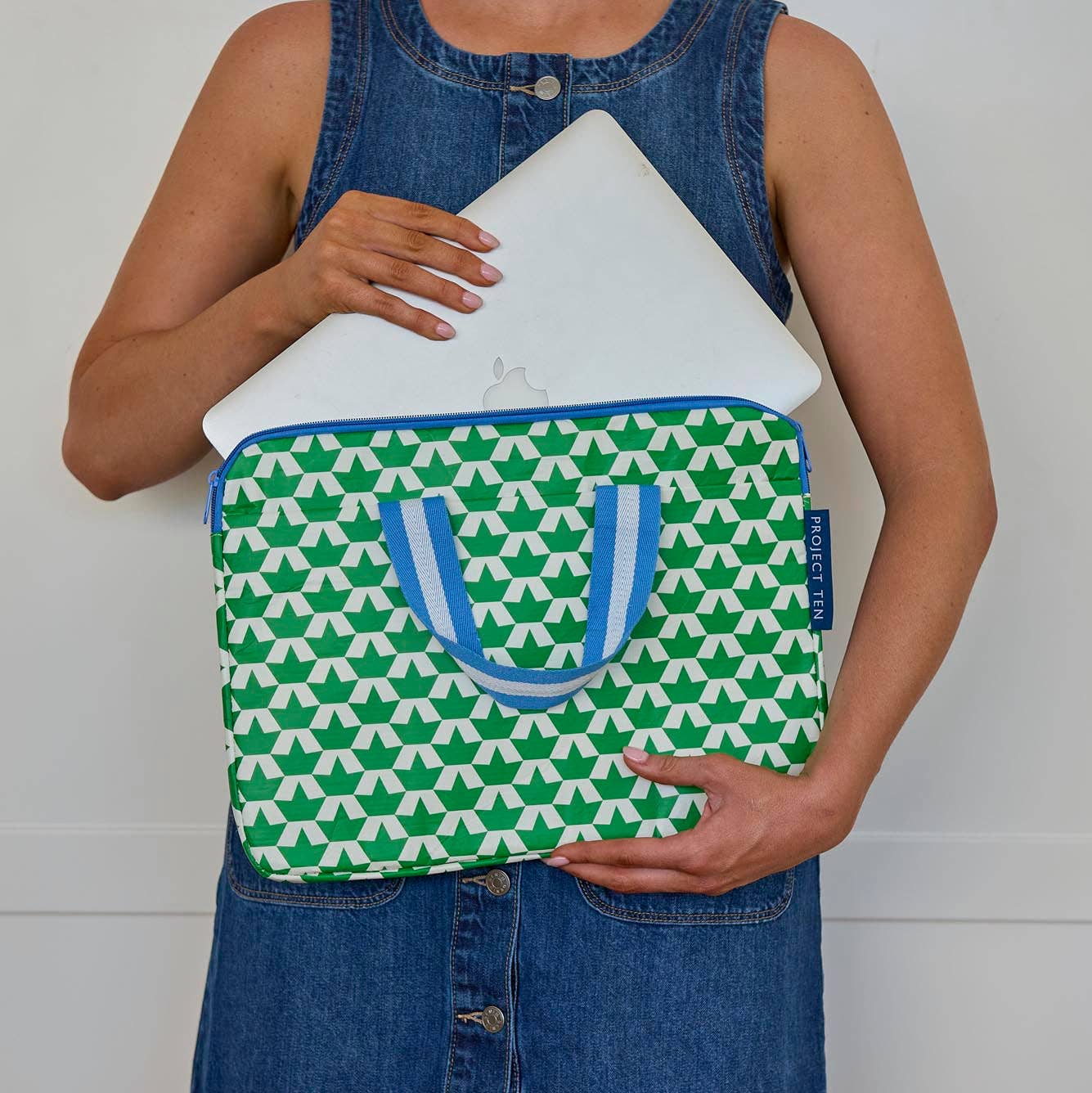 Person holding a green and white patterned laptop sleeve with blue accents.