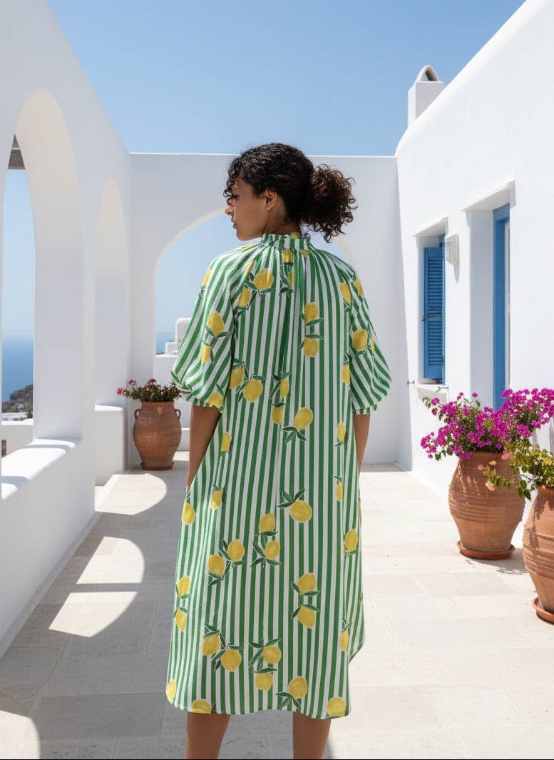 Woman in a green and white striped dress with lemon pattern standing on a sunlit terrace.
