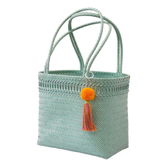 Green woven basket with orange pom-pom and brown tassel on a white background