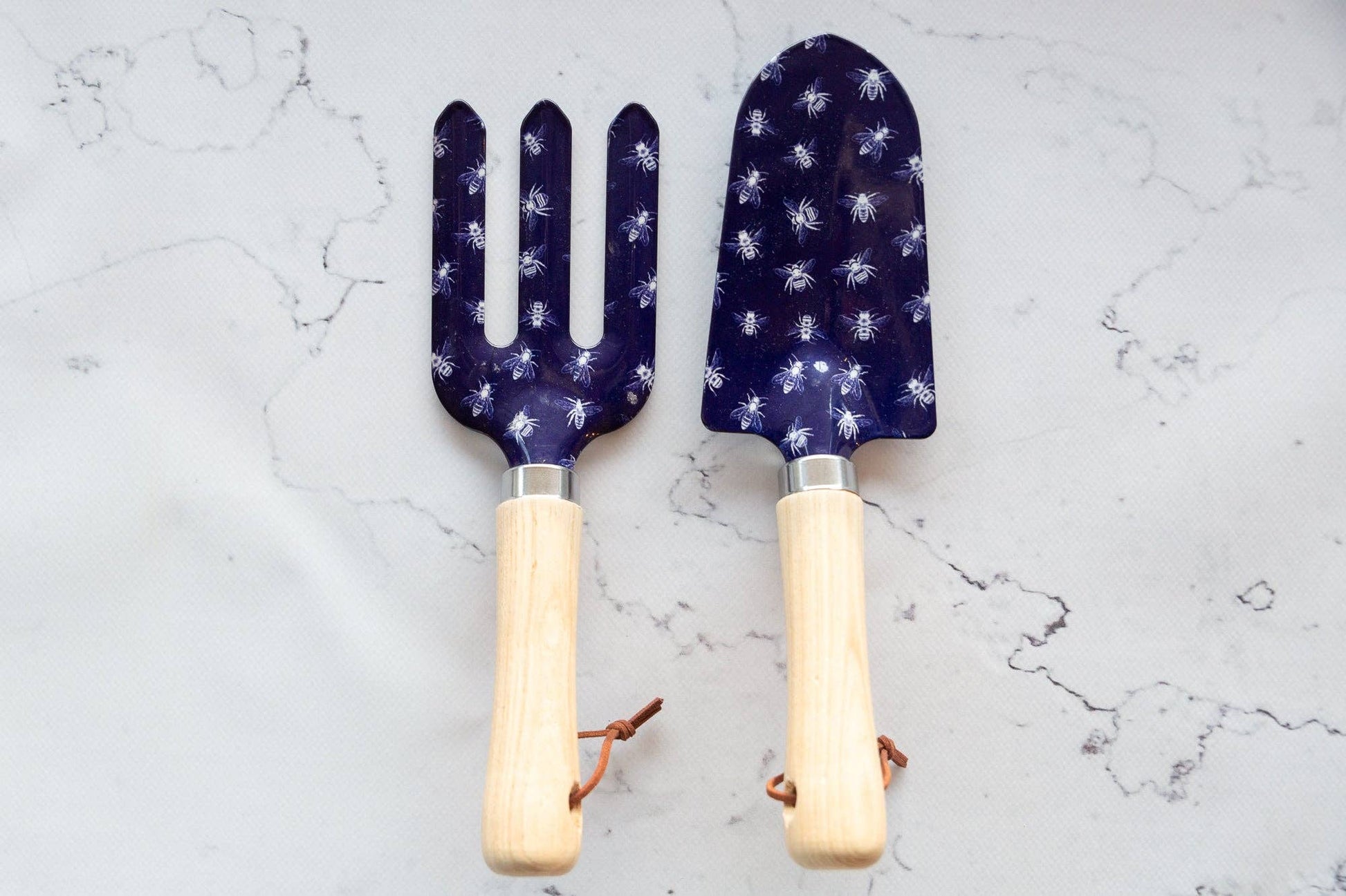 Two gardening tools with blue patterned heads and wooden handles on a light gray marble background.