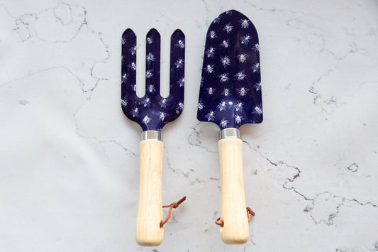 Two gardening tools with blue patterned heads and wooden handles on a light gray marble background.