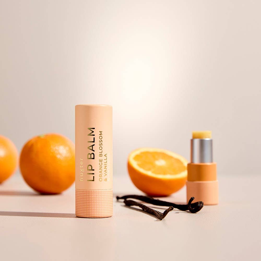 Lip balm with oranges and vanilla beans on a beige background