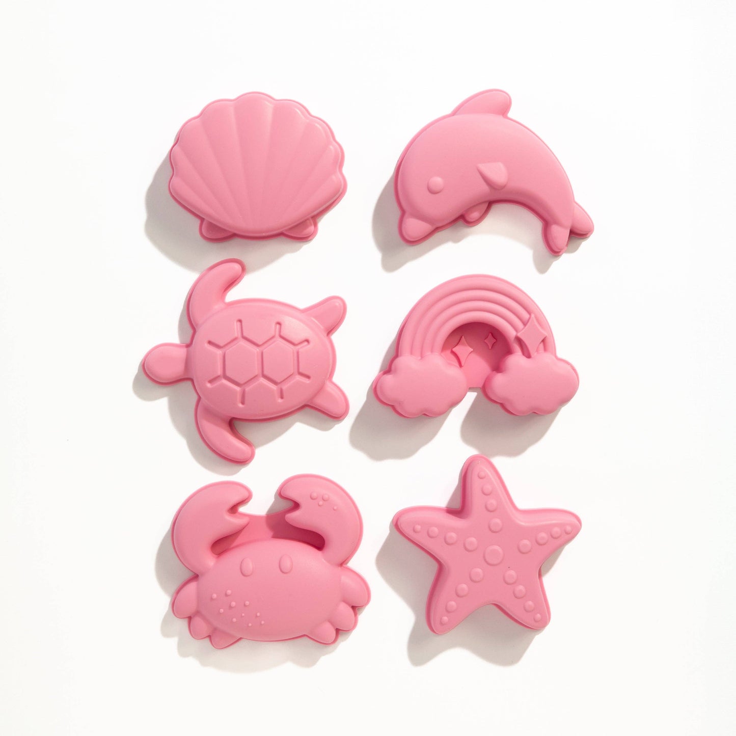 Set of pink silicone beach toys shaped like a shell, dolphin, turtle, rainbow, crab, and starfish on a white background.