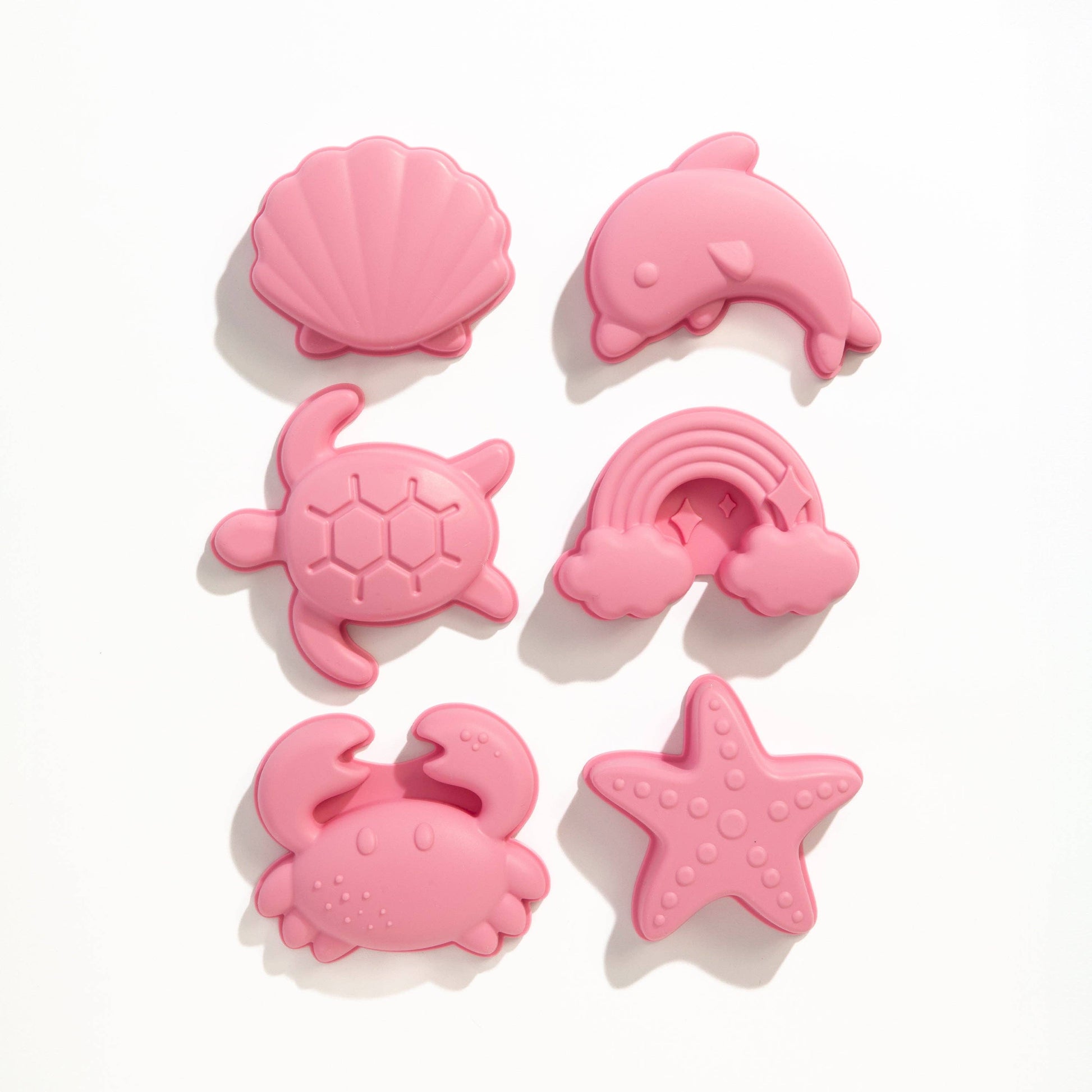 Set of pink silicone beach toys shaped like a shell, dolphin, turtle, rainbow, crab, and starfish on a white background.