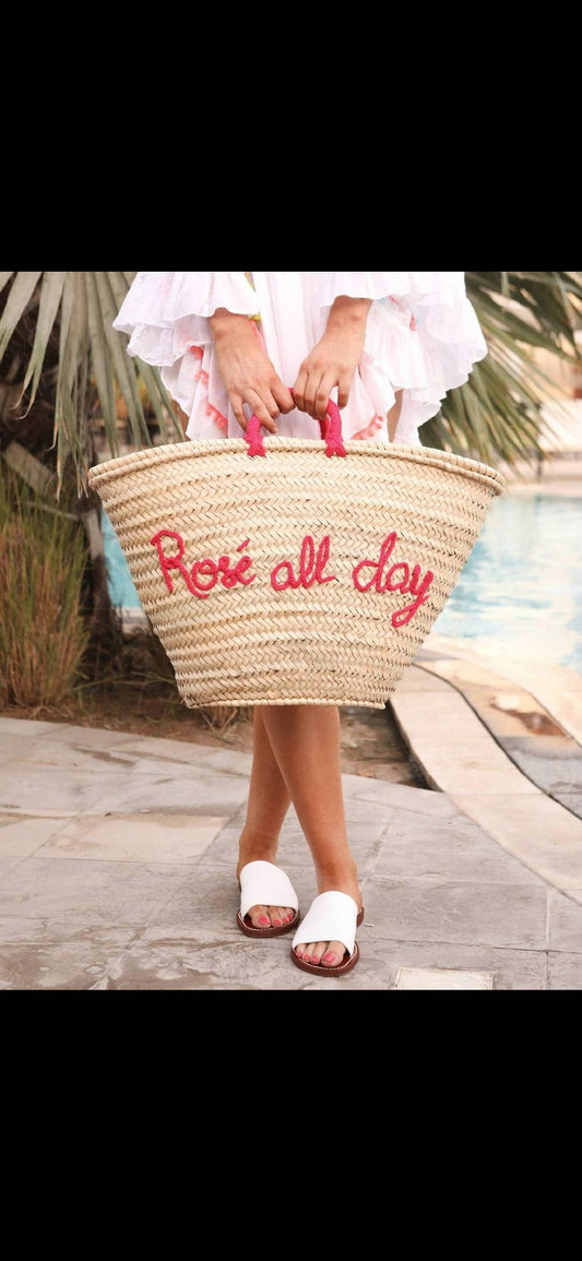 Person holding a straw bag with 'Rose all day' text on a wooden deck.