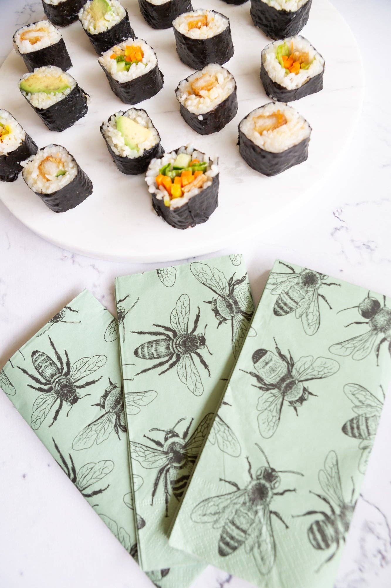 Sushi rolls on a white plate with green paper featuring bee designs.